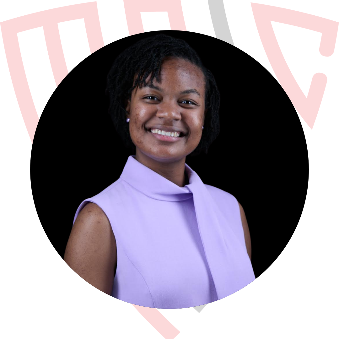 A young woman with braided hair standing at a clear podium, smiling and speaking into a microphone.