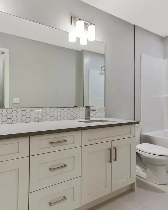 Modern bathroom with white vanity, hexagon tile backsplash, large mirror, and toilet.