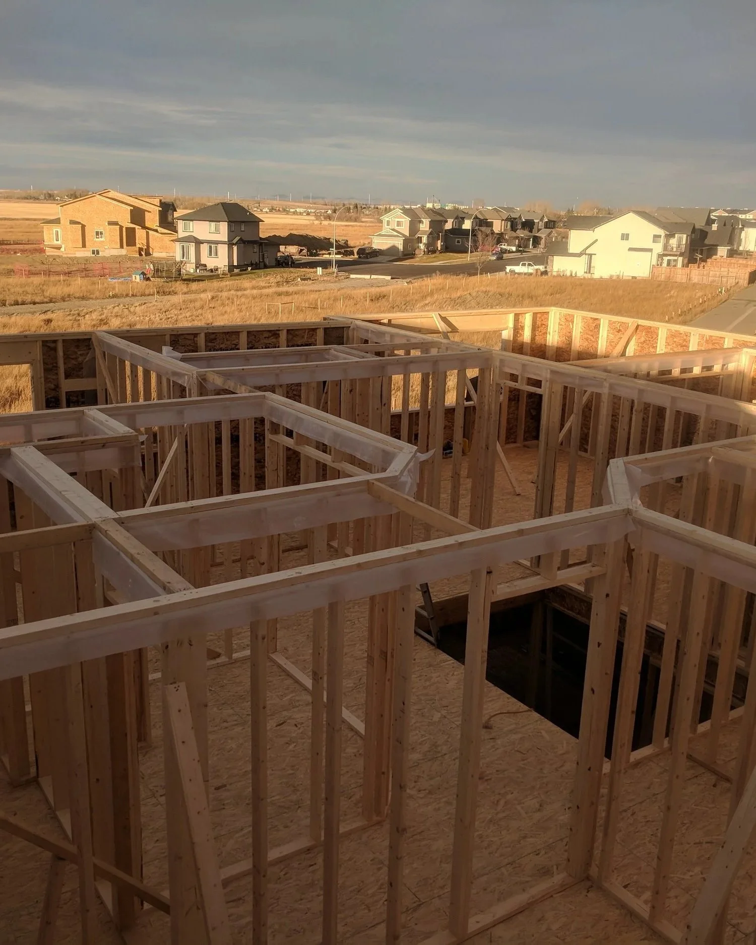 Wooden framing for a house under construction with a suburban neighborhood visible in the background.