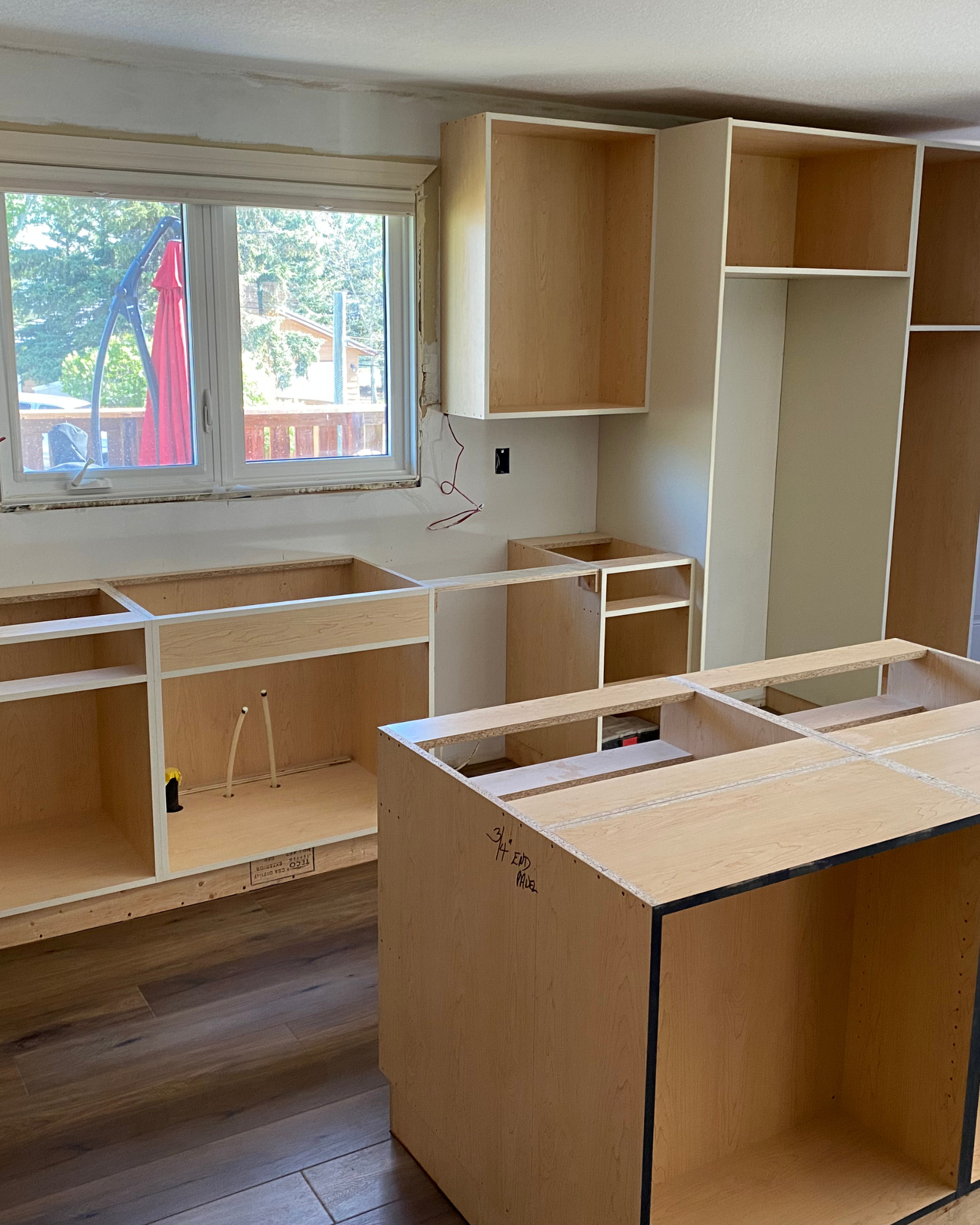 Kitchen with unfinished cabinetry and cabinets under construction, window overlooking outdoor patio and garden.