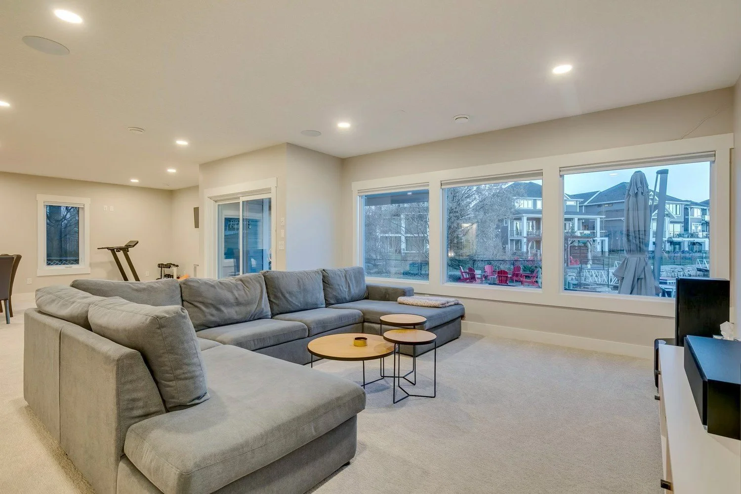 Spacious living room with large windows, gray sectional sofa, and small round coffee tables with black legs.