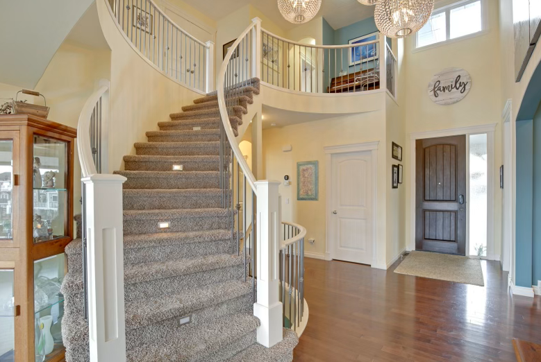 View of a home's foyer with a curved staircase, hardwood floors, a dark front door, and a sign that says 'family' on the wall.