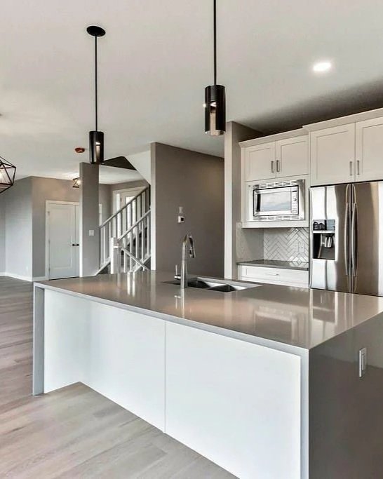 Modern kitchen with white cabinets, stainless steel refrigerator, microwave, and a large island with a sink, pendant lighting, and light-colored wood flooring.