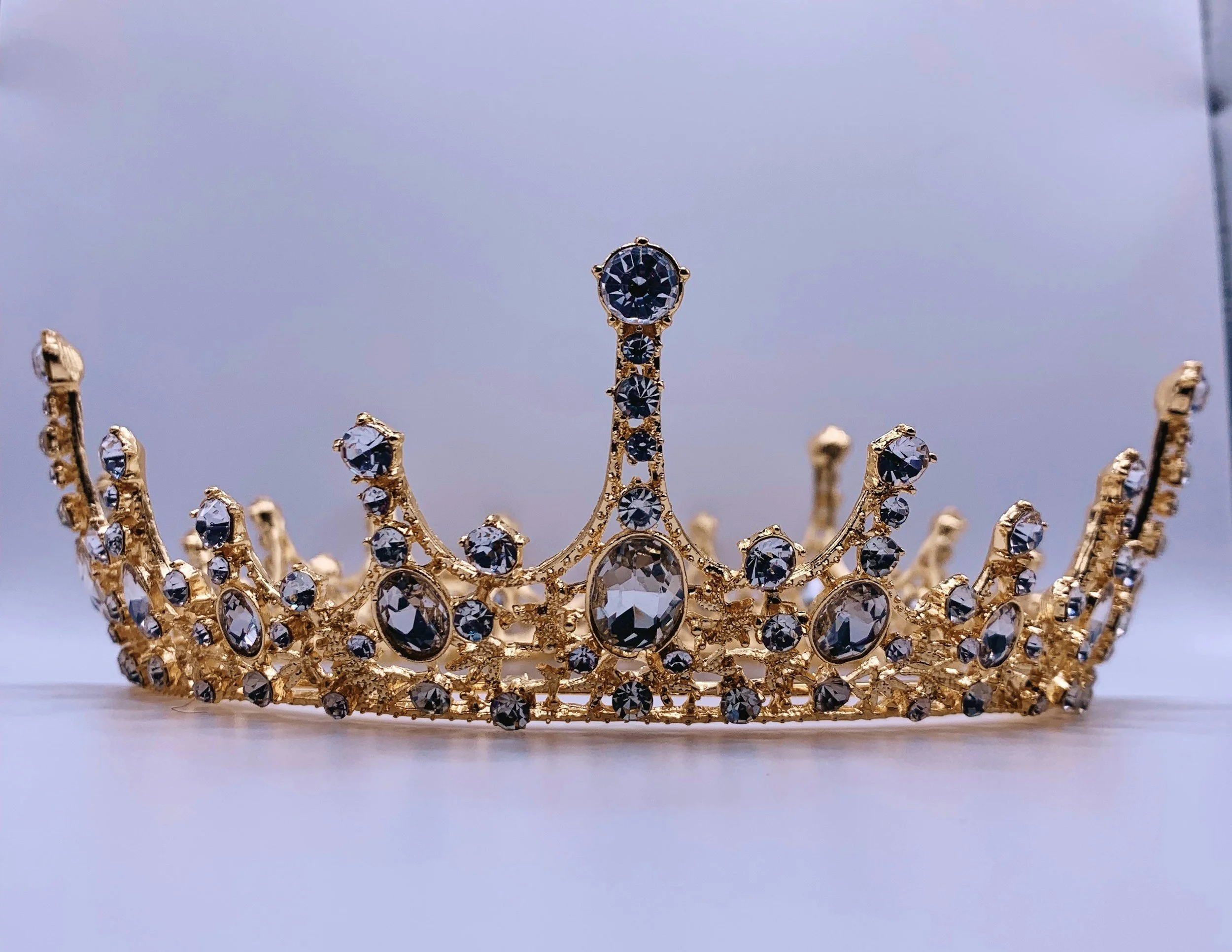 A gold tiara or crown decorated with numerous black and clear gemstones, displayed on a white surface.