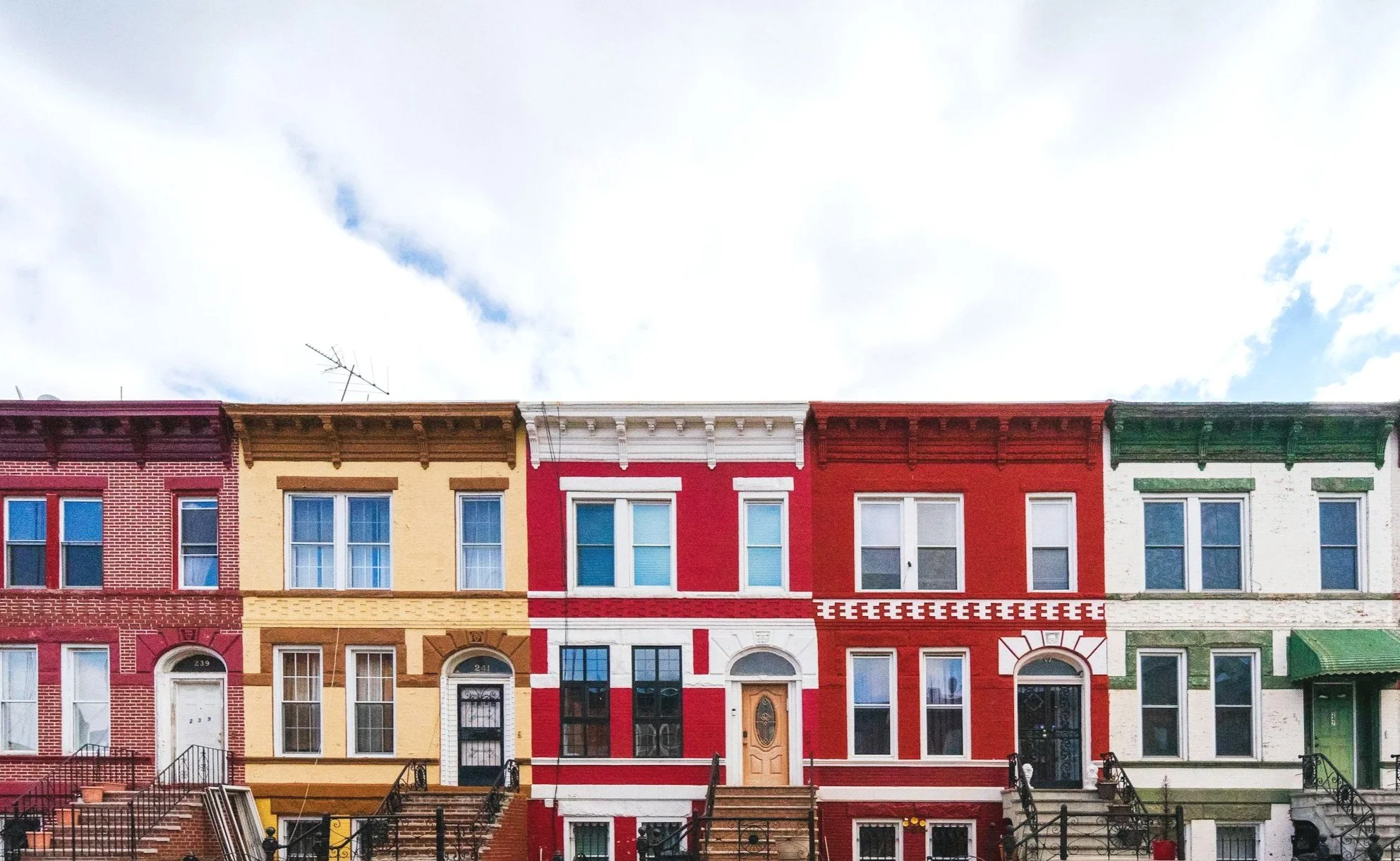 Colorful row houses in Baltimore's Federal Hill neighborhood, featuring painted brick facades in red, yellow, white, and green with front steps and staircases.