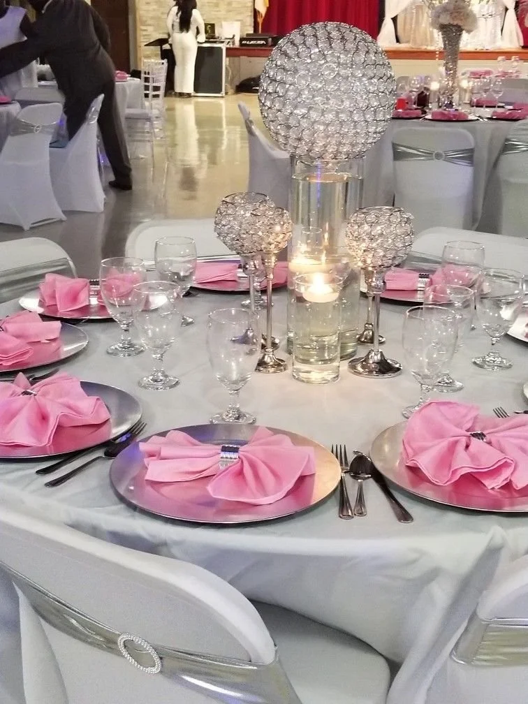 Elegant banquet table decorated with pink napkins, glassware, and crystal centerpieces, set for a formal event or wedding reception.