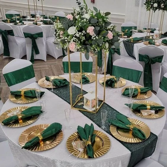 Elegant banquet table decorated with white tablecloth, gold and green accents, and a tall floral centerpiece with pink and white flowers and greenery.