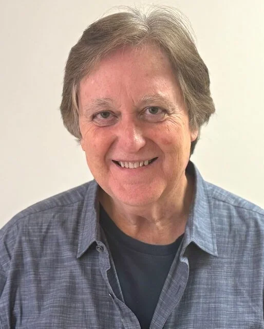 Close-up of a smiling man with light brown hair, outdoors.