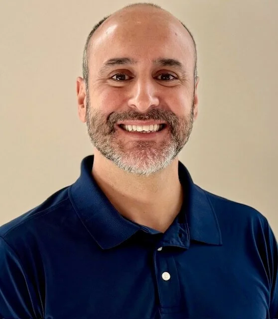 A smiling man standing next to a blackboard with the word 'Thrive' written on it in green script.