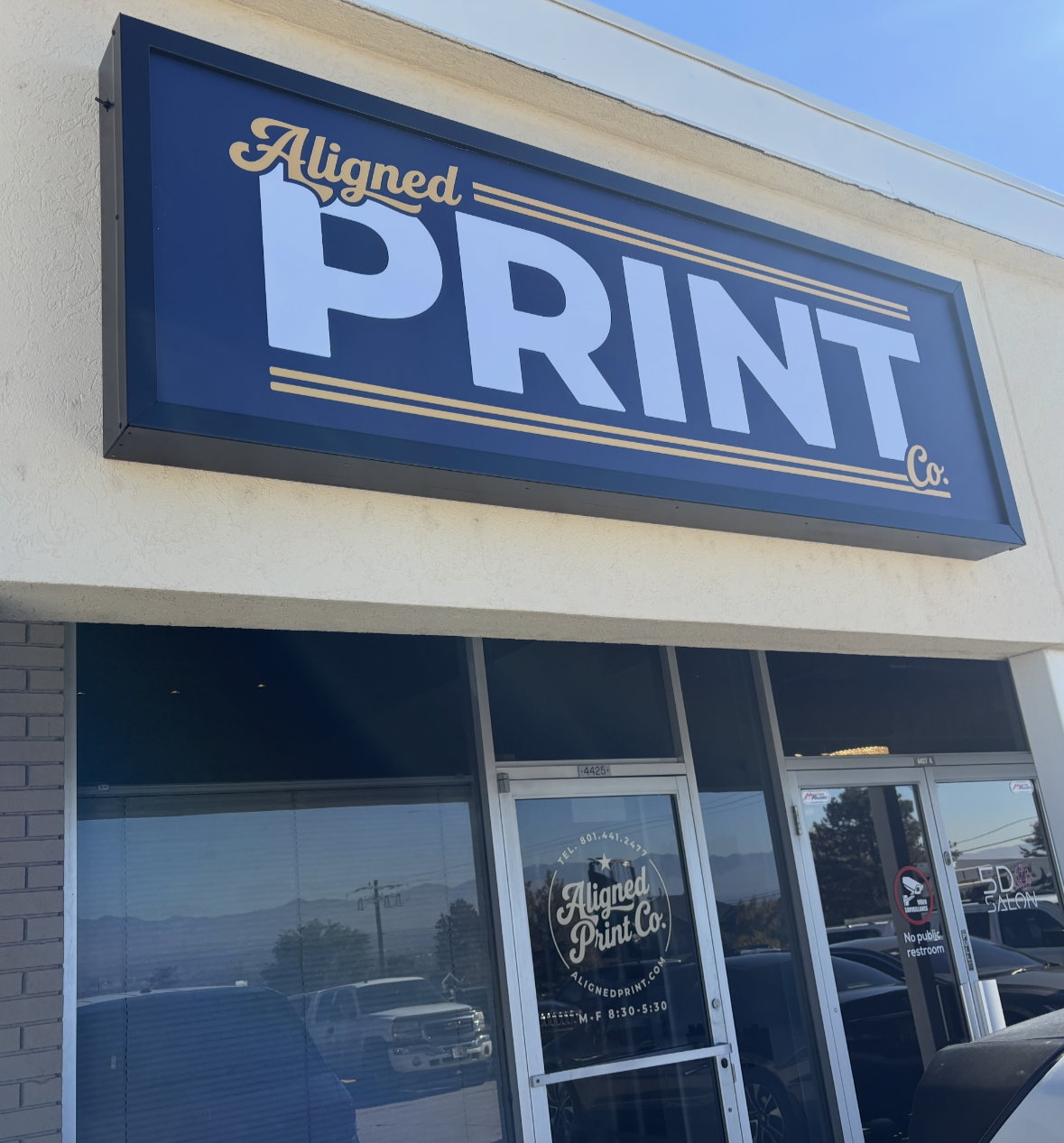 Print and copy shop signage on building that says Aligned Print Co. in white and gold letters on a dark blue background.