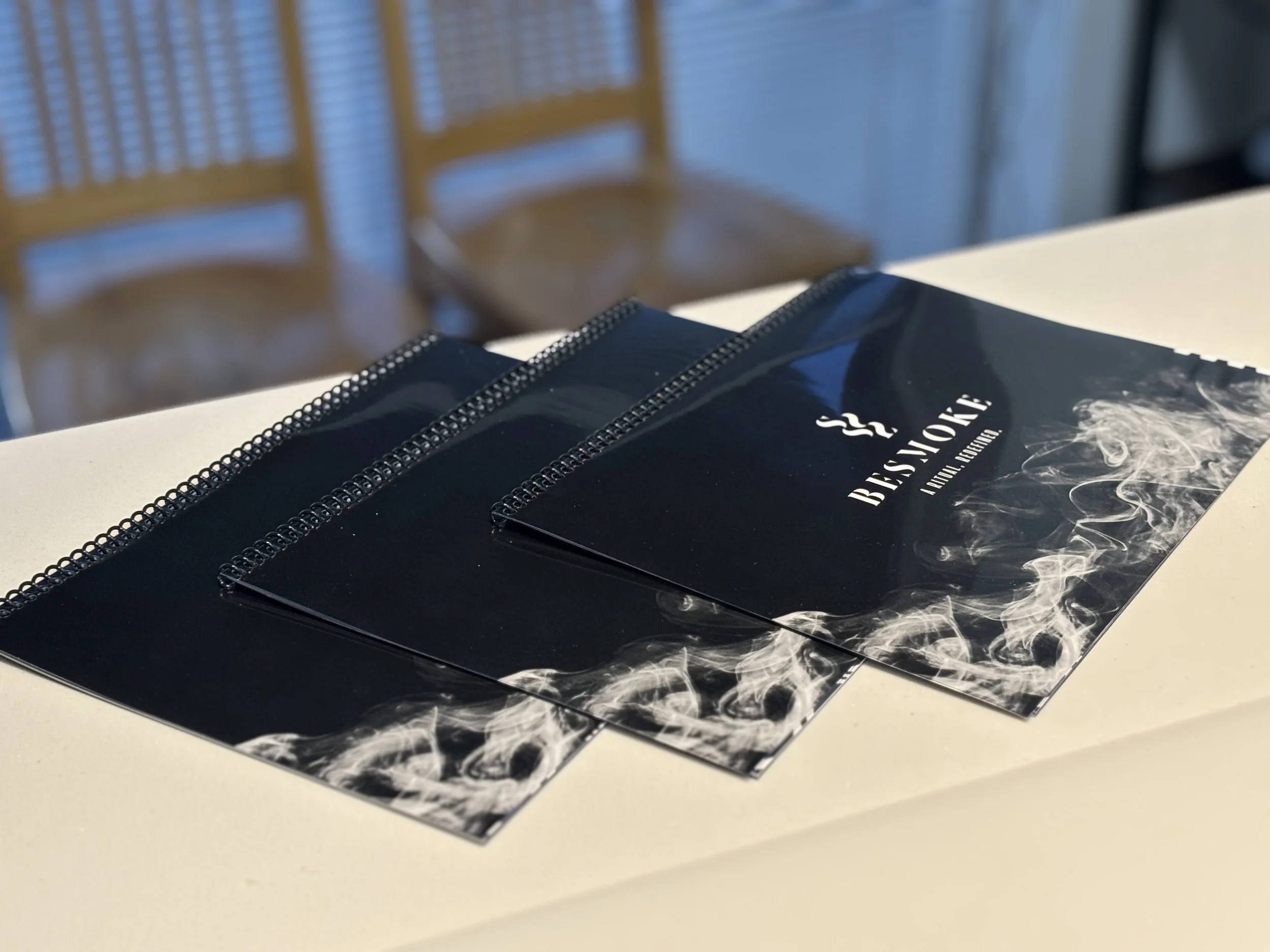 three printed product booklets or brochures sitting on a counter top with two chairs in the background