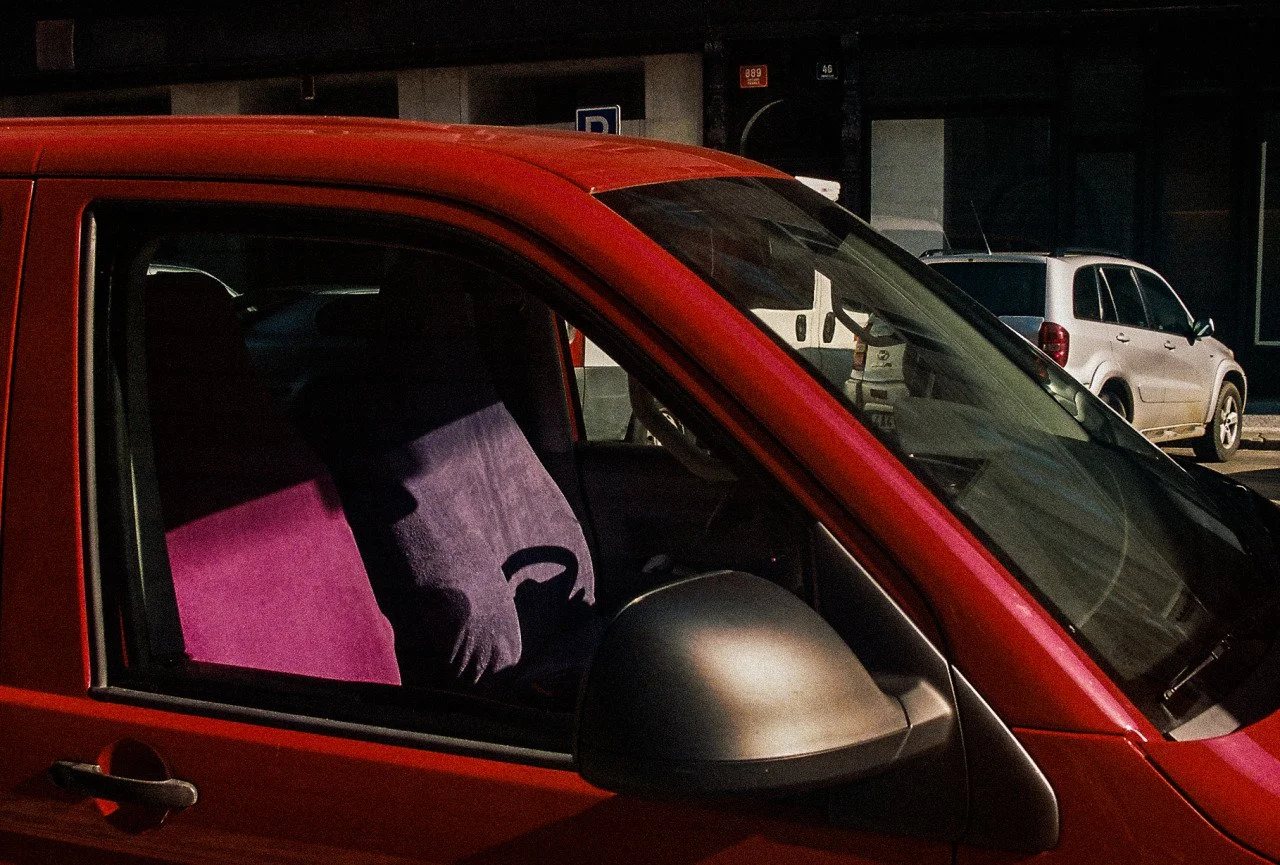 Close-up of a red car with purple seat covers inside, parked in a parking lot during nighttime, with other vehicles visible in the background.