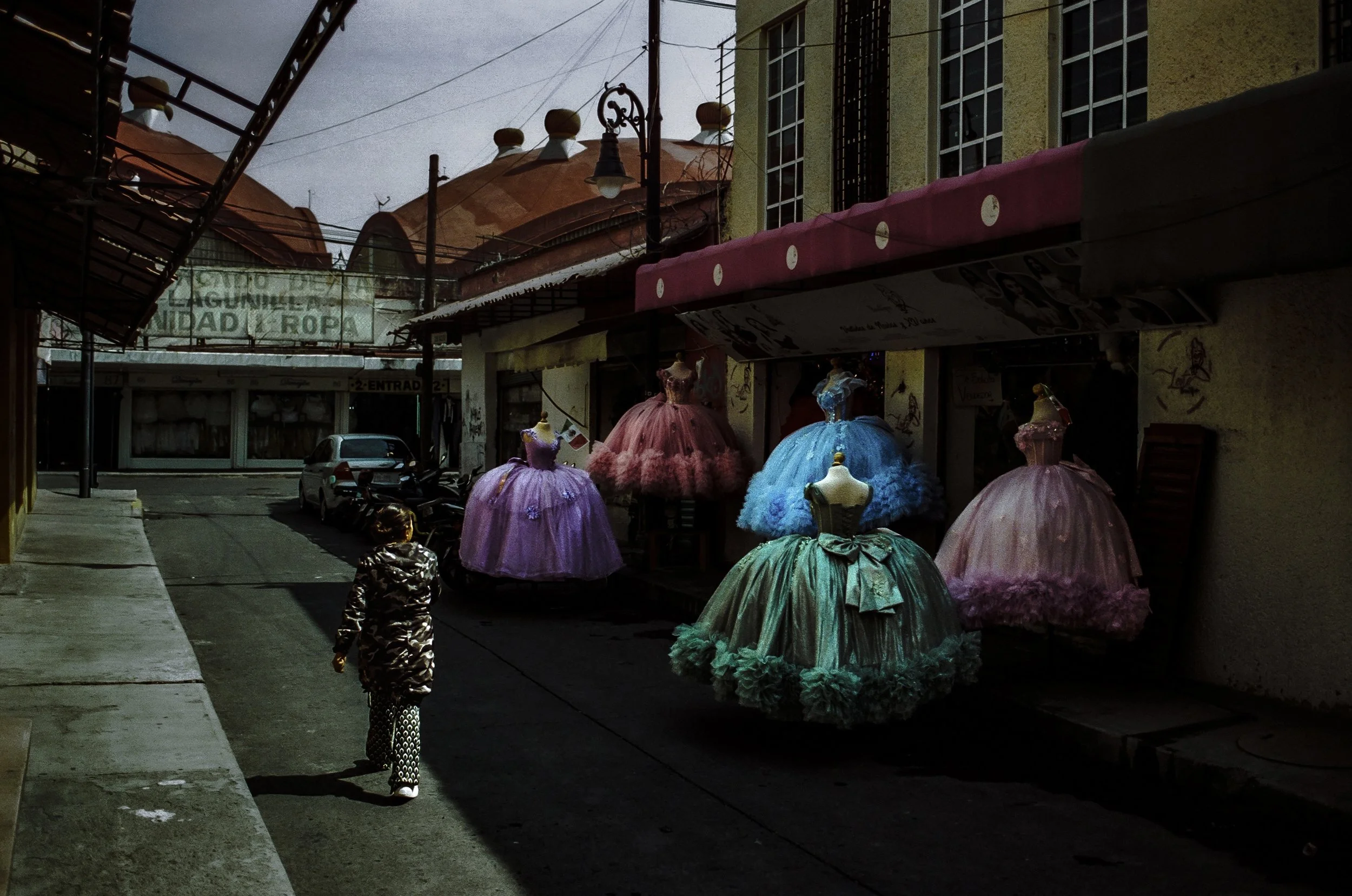 Street scene with colorful ball gowns displayed outside a shop, and a child walking on the sidewalk.