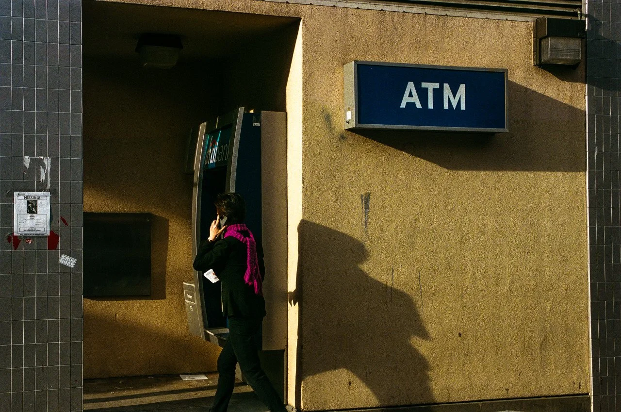 A woman talking on a mobile phone near an ATM outside a building.