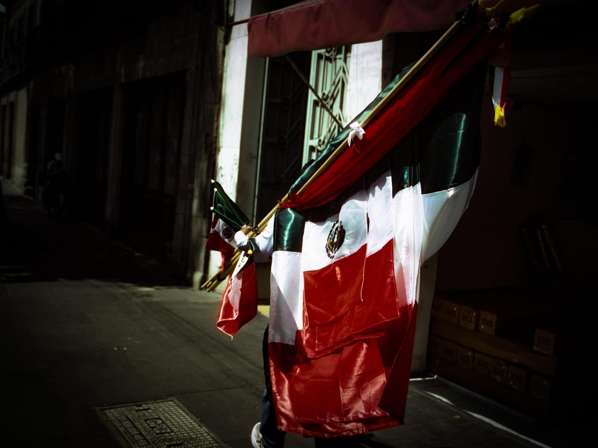 A person wearing a red and white flag draped around their shoulders, standing in a dimly lit indoor space with a metal grille floor and stacked boxes on the right.