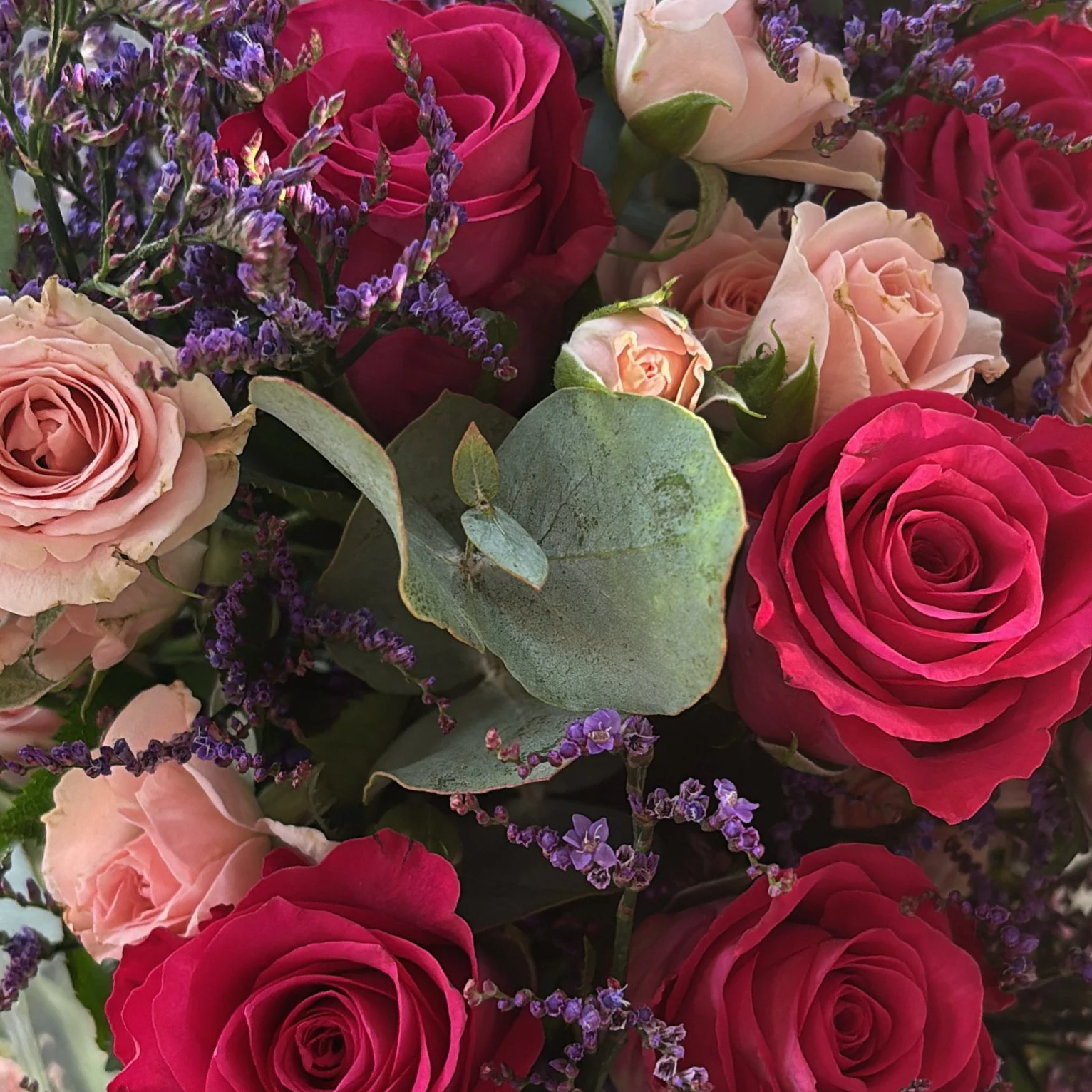 A close-up of a bouquet with pink, peach, and red roses, accented with purple lavender and green leaves.