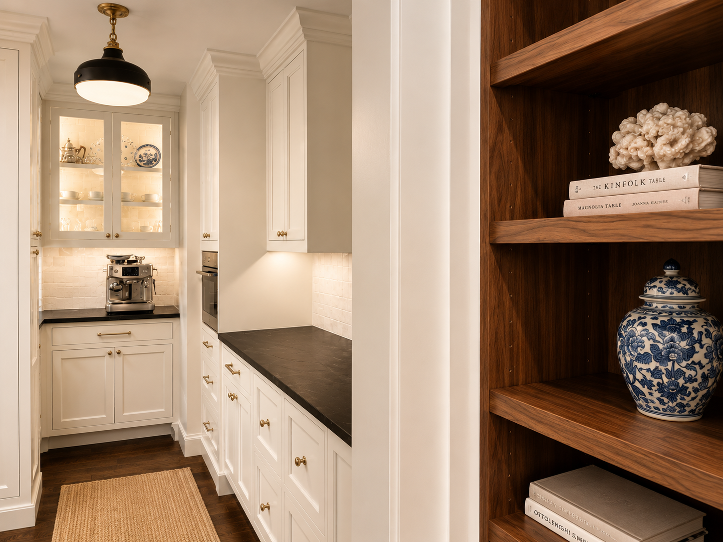 A narrow hallway with built-in white cabinetry on both sides and a beige rug on the wooden floor, leading to a kitchen area with white cabinets and a pendant light overhead.