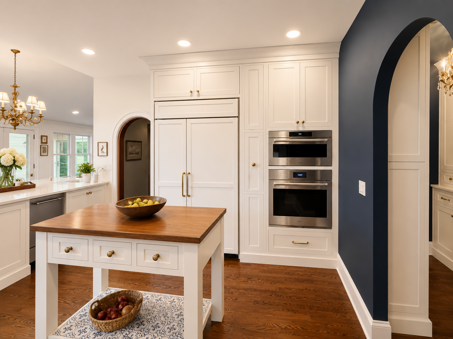 Spacious kitchen with white cabinets, wooden countertops, and hardwood floors, featuring a central island, a chandelier, and large windows with views of trees outside.