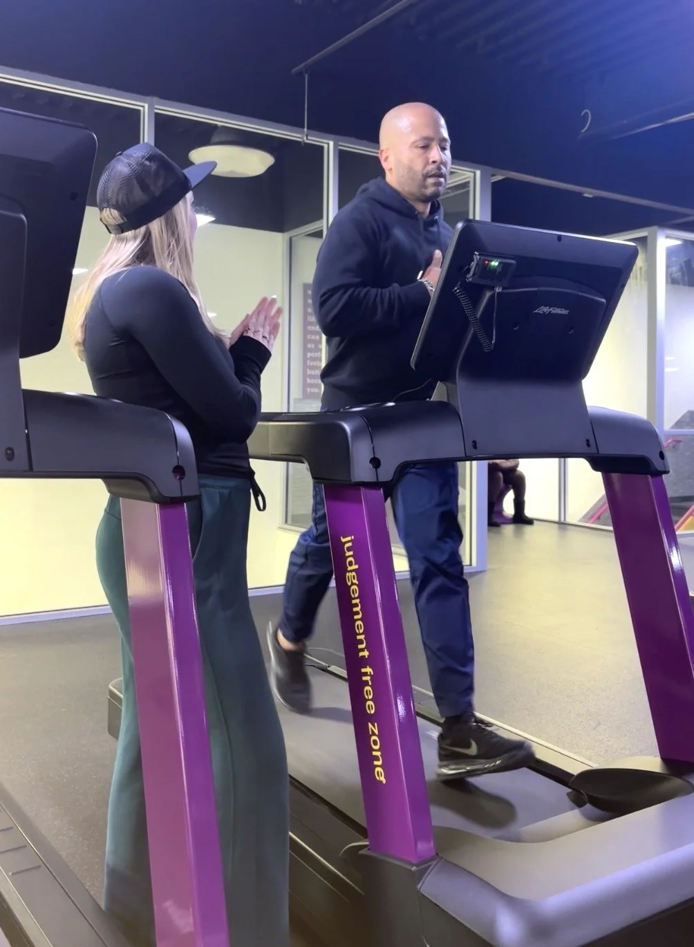A man running on a treadmill while a personal trainer provides encouragement from the side.