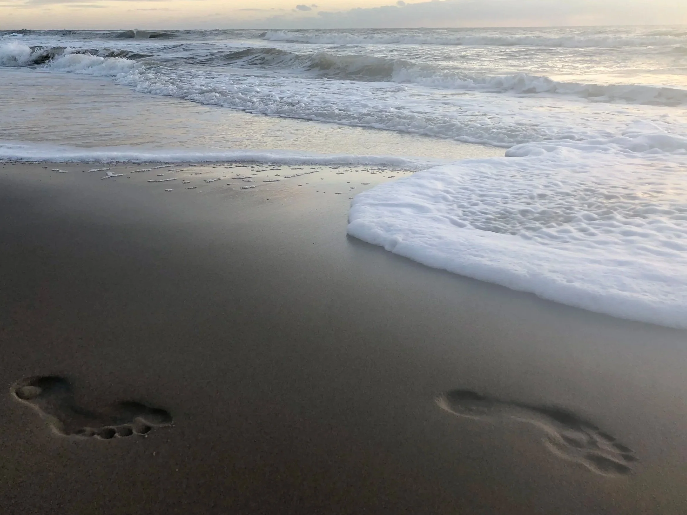 Sandstrand mit footprints, Meereswellen und bewölktem Himmel.