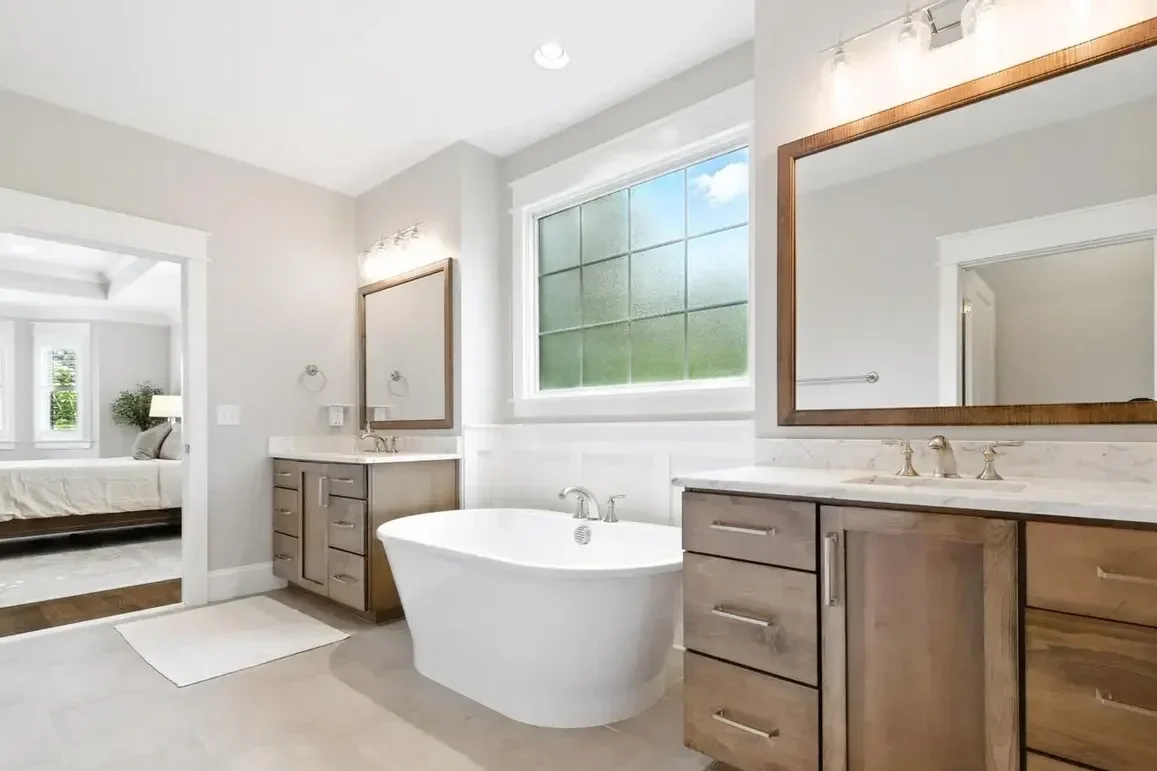 Modern bathroom with a freestanding bathtub, two wooden vanities with mirrors, and a large window with green view.