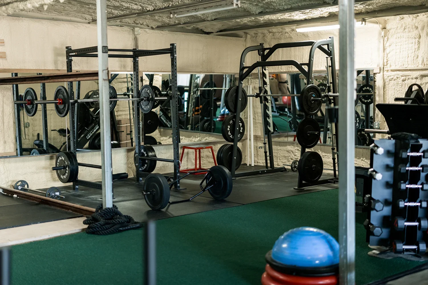 Empty gym with weightlifting equipment, mirrors, and workout accessories, including barbells, weights, and a BOSU ball.