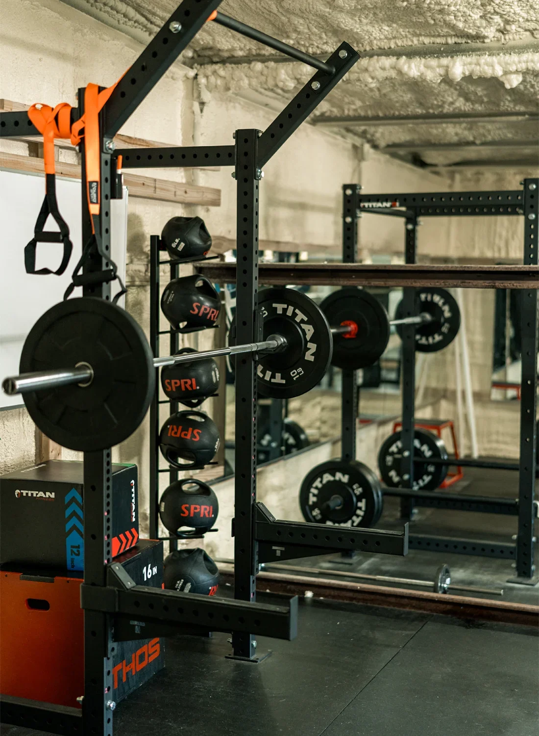 A home gym with weightlifting equipment, including barbells, weight plates, medicine balls, and a squat rack.