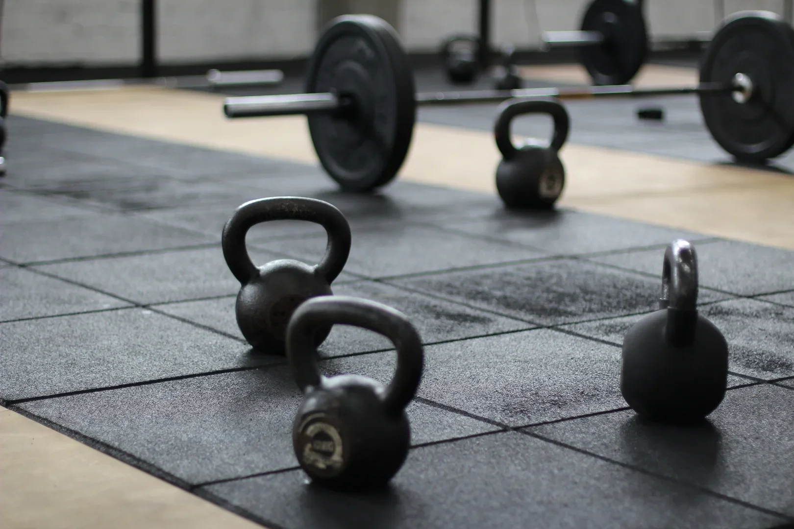 Kettlebells and a barbell on a gym floor with rubber mats.