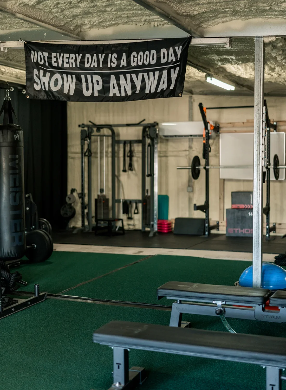 Interior of a gym with workout equipment, barbells, rowing machines, and a banner hanging from the ceiling that reads, "Not every day is a good day. Show up anyway."