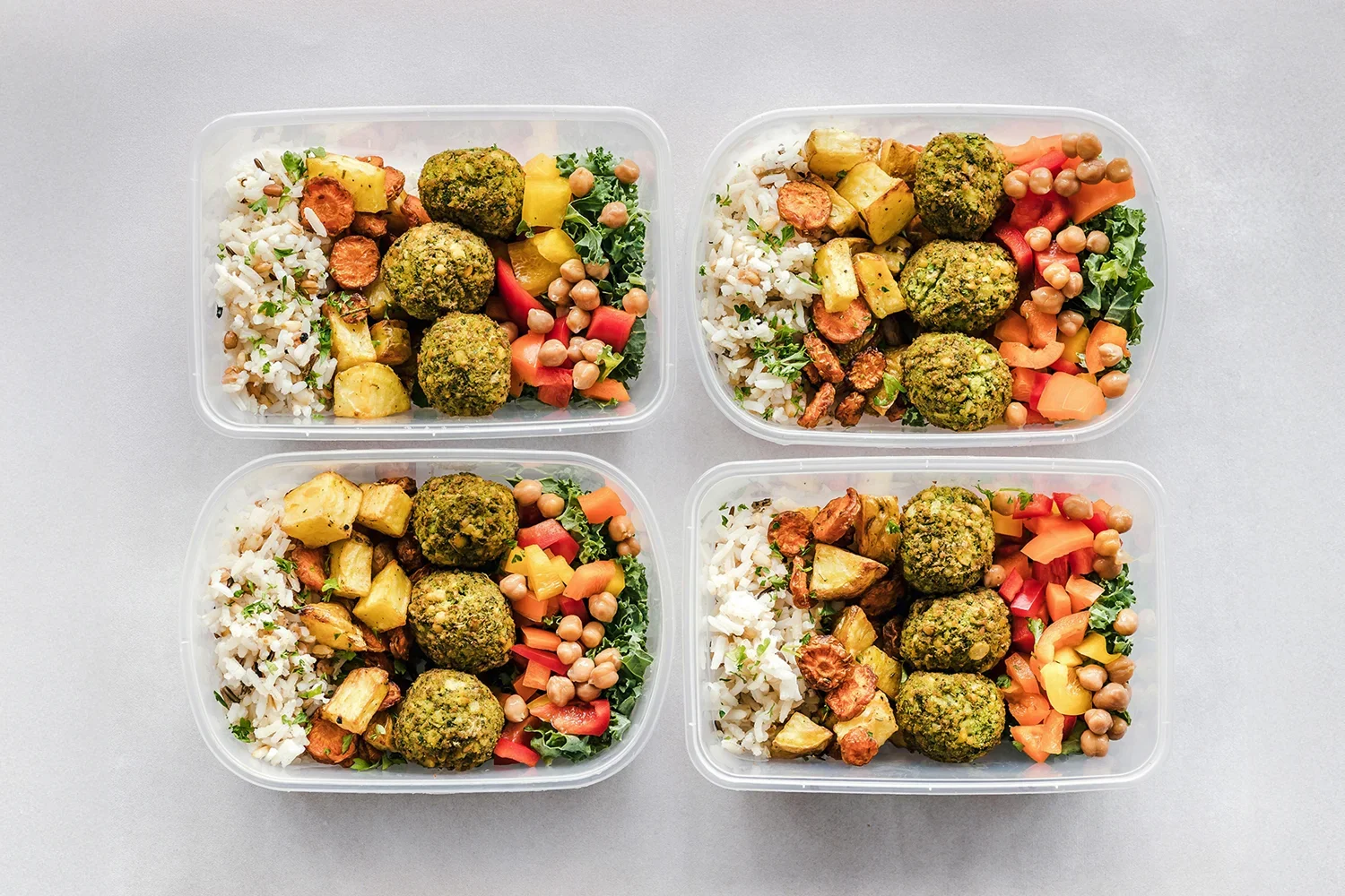 Four meal prep containers with rice, roasted vegetables, chickpeas, and falafel