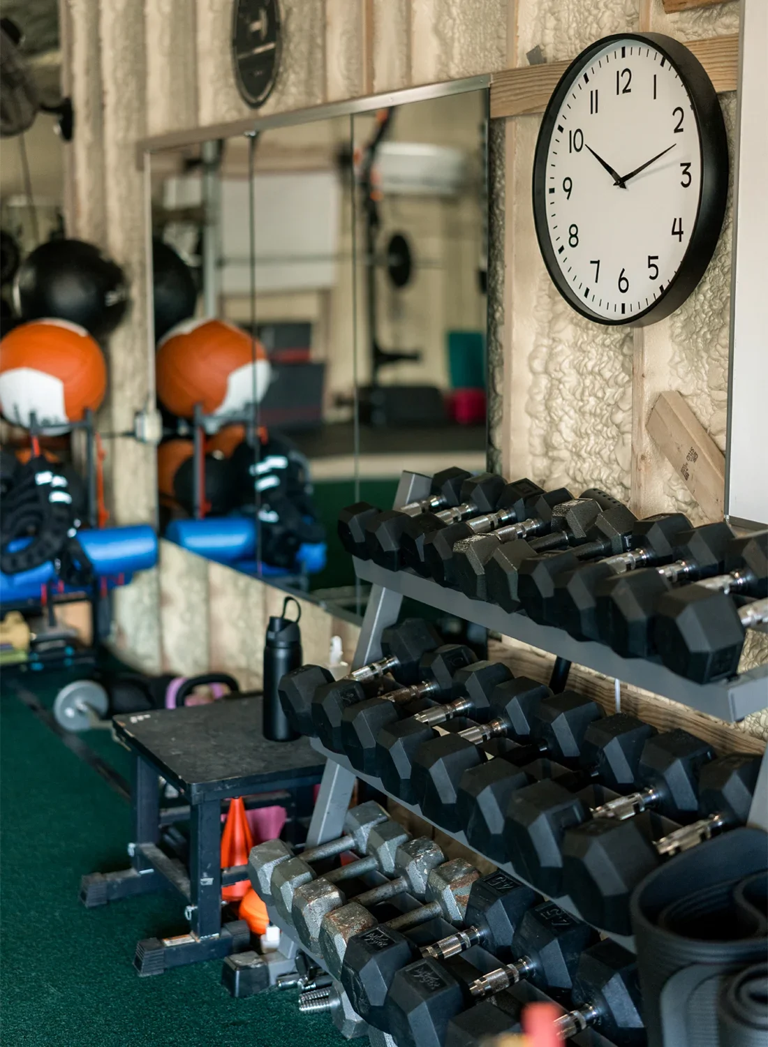 Dumbbell rack with black dumbbells in gym, wall clock, mirror, and gym equipment in background