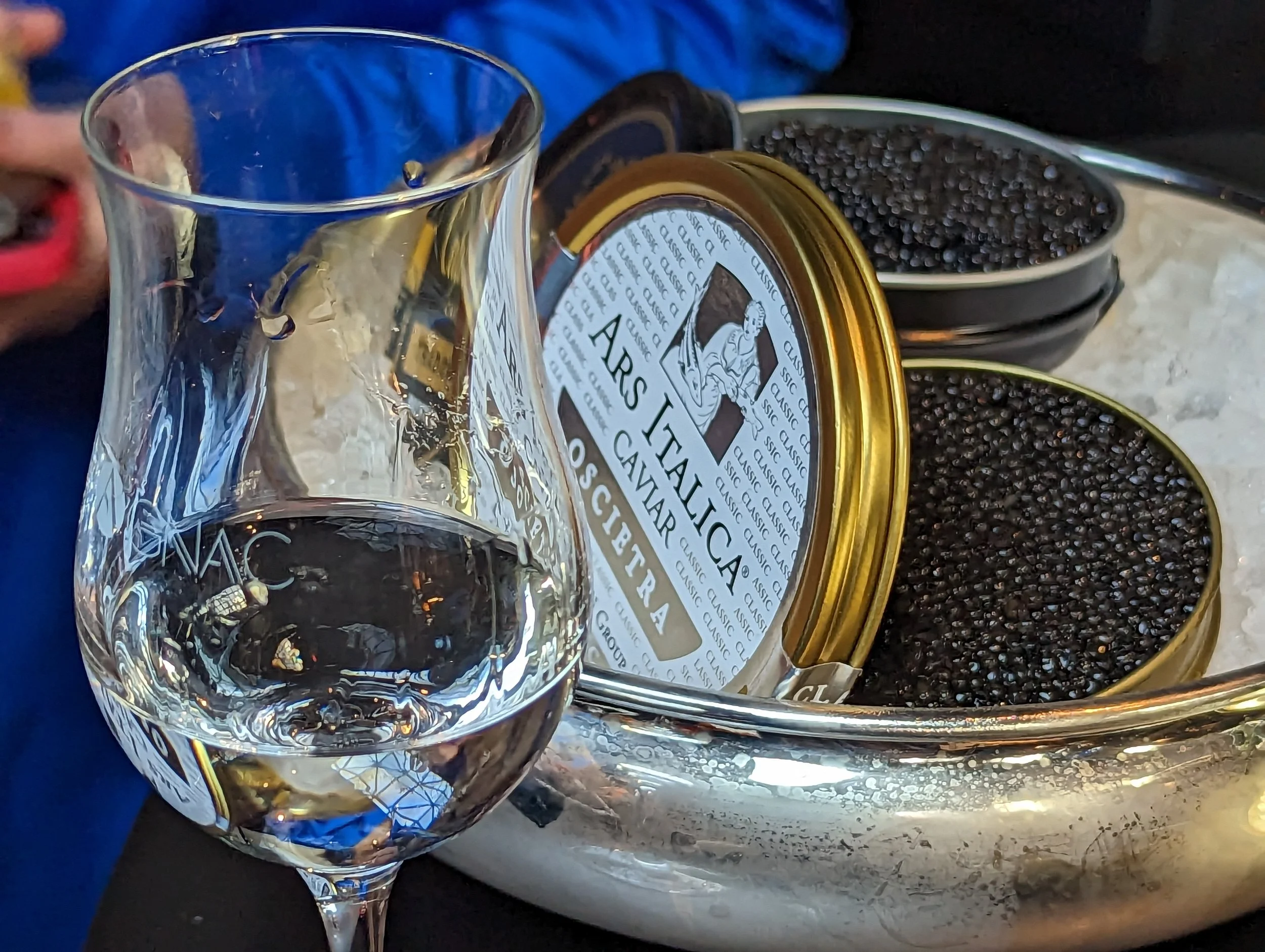 A glass of clear water placed next to open tins of black caviar on a silver tray.