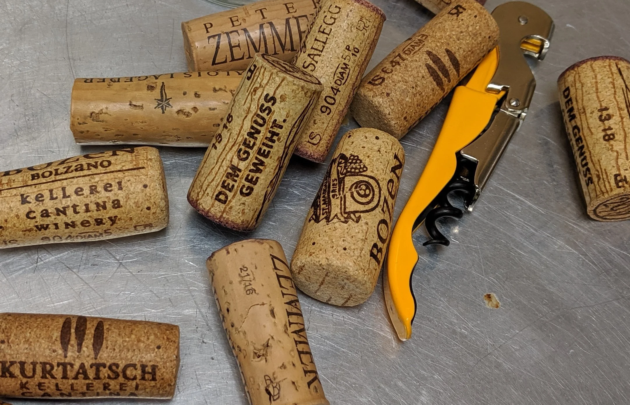 Multiple wine corks and a yellow corkscrew on a metallic surface.