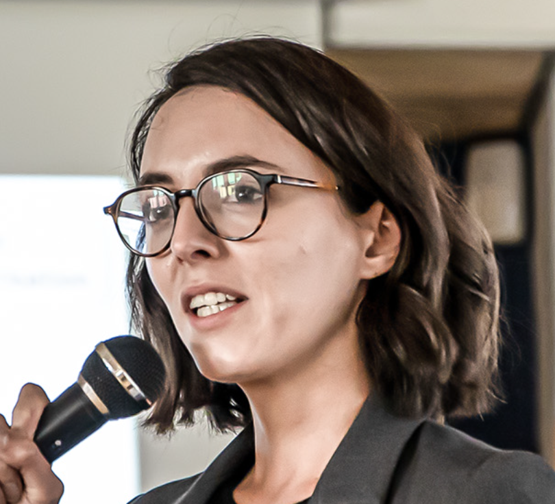 A woman with short dark hair and glasses speaking into a microphone.