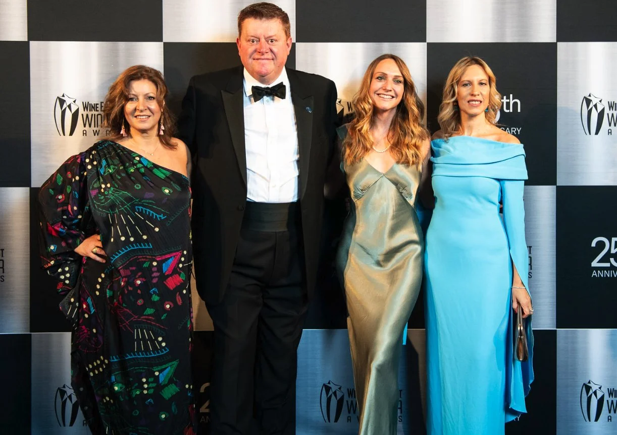 Four individuals in formal attire posing on a black and white checkered backdrop at the 25th anniversary Wine Enthusiast Wine Awards event.