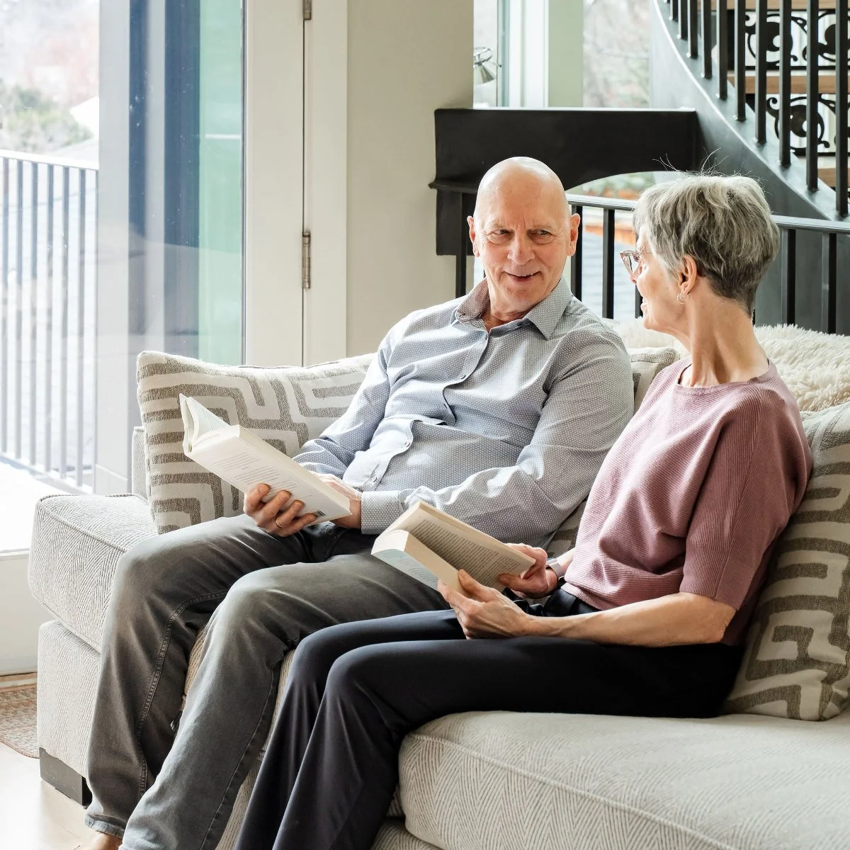 Two older adults reading a book together at home