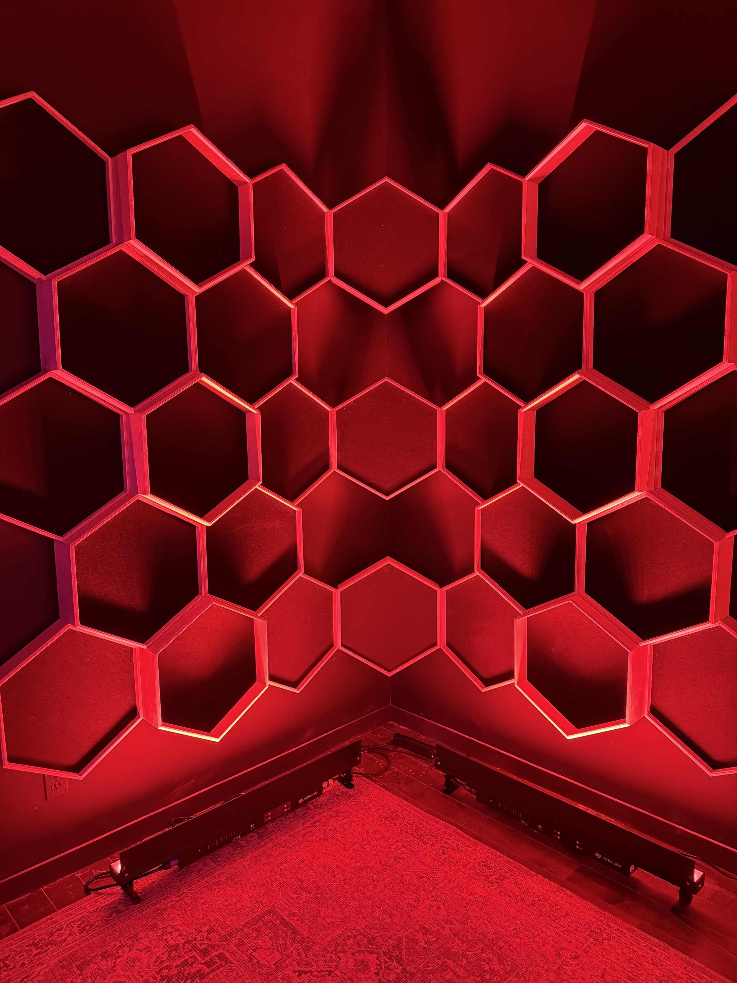 Red hexagonal LED light installation on a corner wall with a carpeted floor.