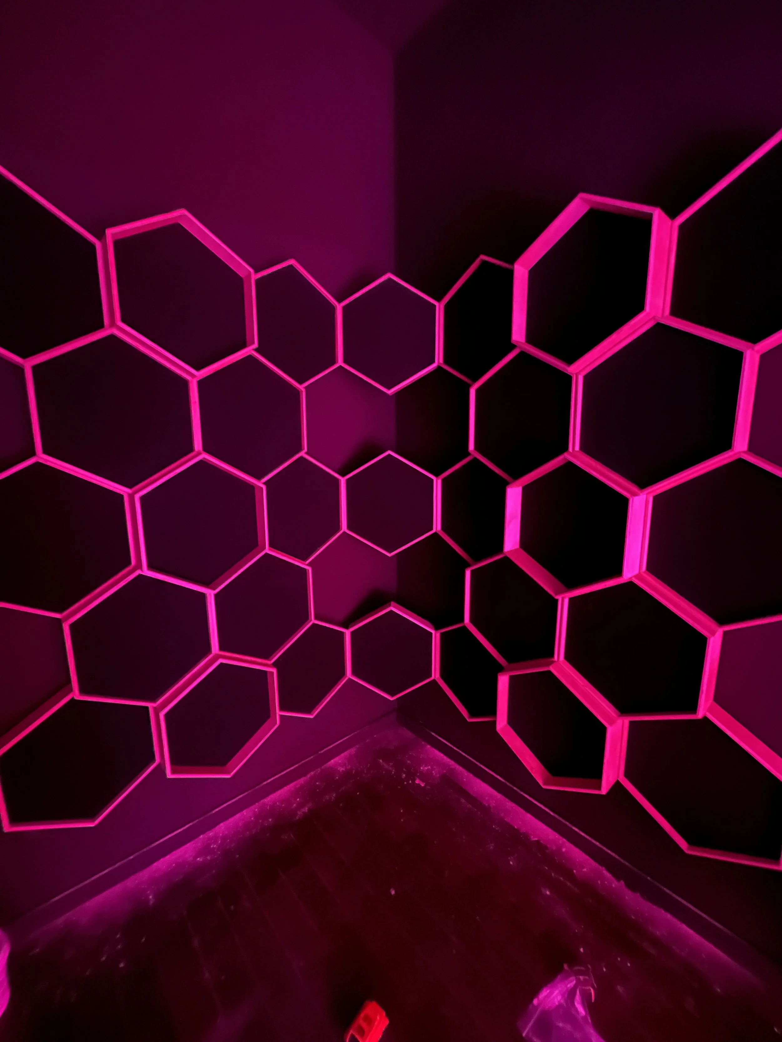 Wall with illuminated pink hexagon pattern on a dark background.