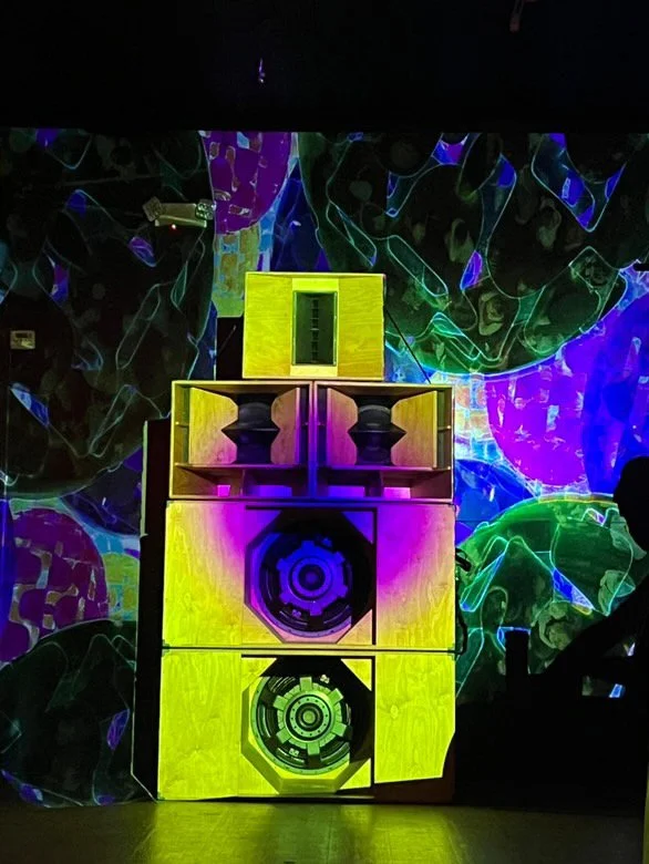 A set of large speakers with colorful lighting effects and a vibrant, abstract digital background.