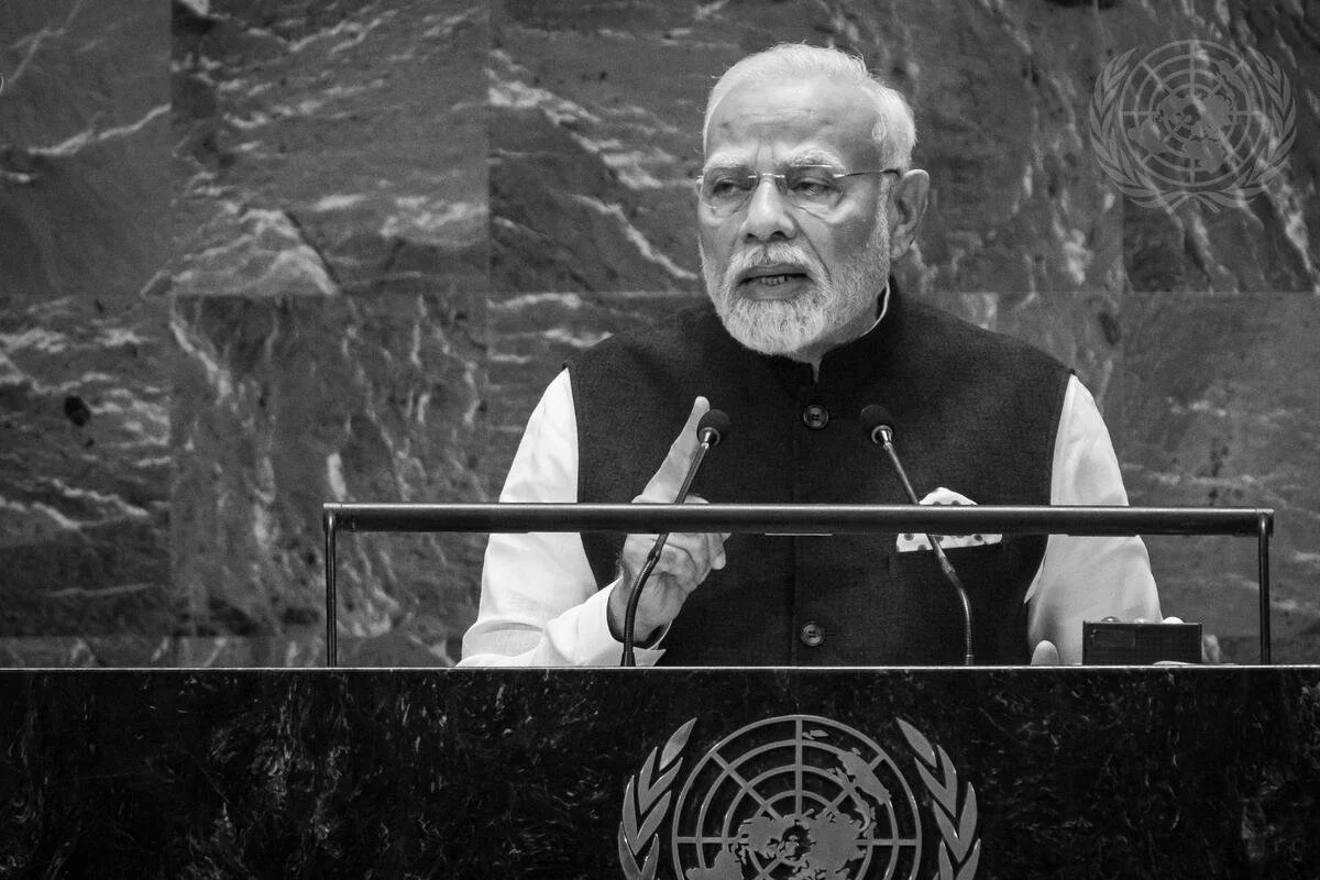 Indian Prime Minister Narendra Modi speaking at the United Nations, standing behind a podium with the UN emblem, gesturing with his right hand.