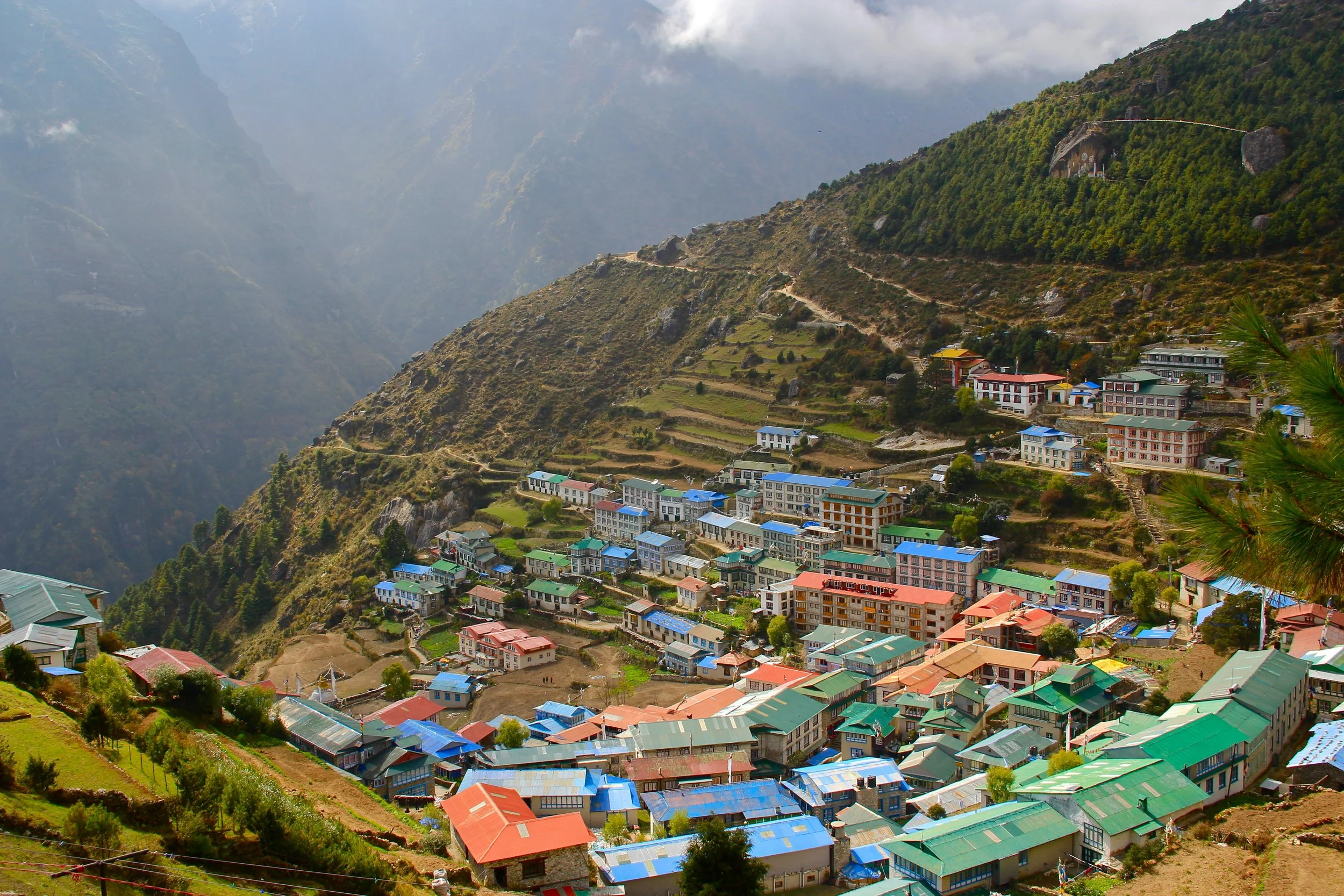 A mountain village with colorful buildings and green terraces on a hillside, surrounded by misty mountains.