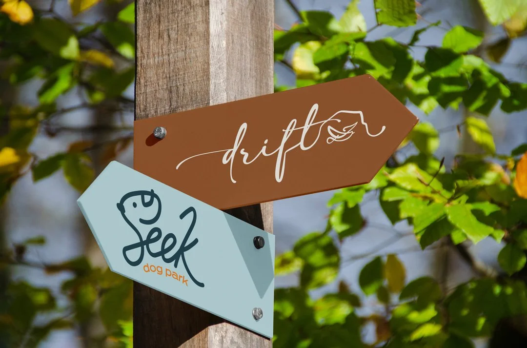 Signpost with two signs, one labeled 'drift' and the other labeled 'Seek dog park', attached to a wooden post amid green foliage.