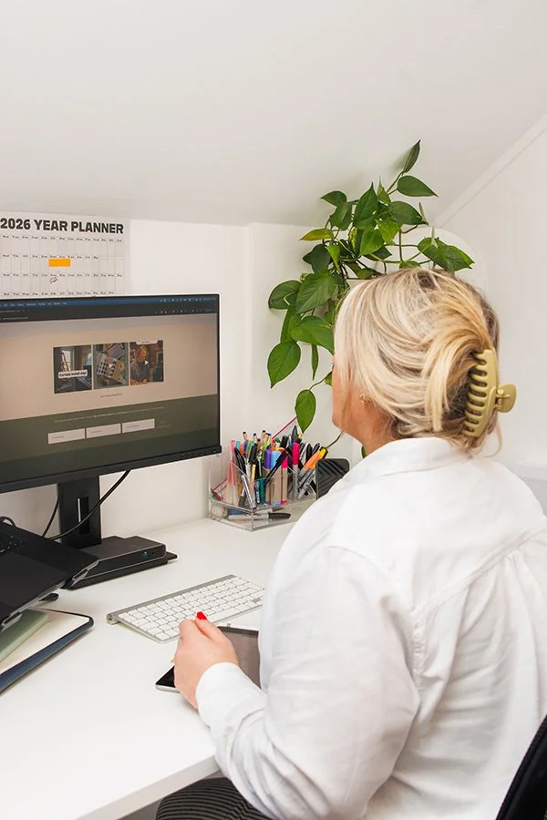 Woman with blonde hair in a hair clip working at a desk with computer and supplies.