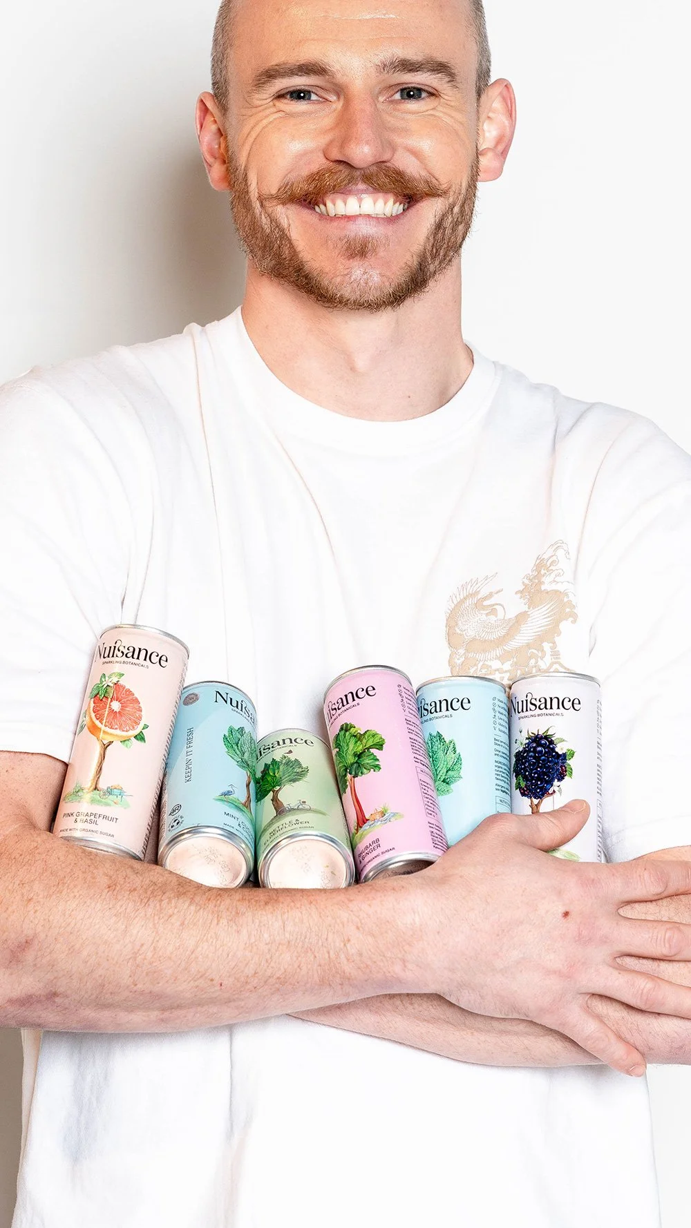 full nuisance drinks range held in crossed arms by smiling man with moustache