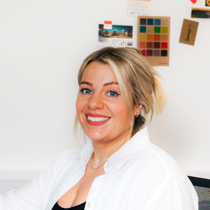 Sarah Wardlaw, Creative Director and founder smiling, seated in an office with colorful art on the wall behind her.