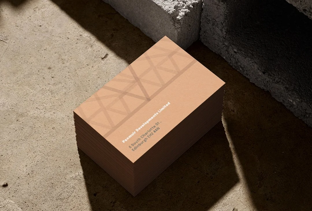 A stack of business cards on a concrete surface next to a brick wall, displaying the name 'Panmuir Development Limited' and an address in Edinburgh, Scotland.