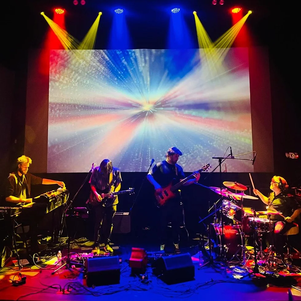 Band performing on stage at the Double E VT with colorful lights and a space-themed digital backdrop.