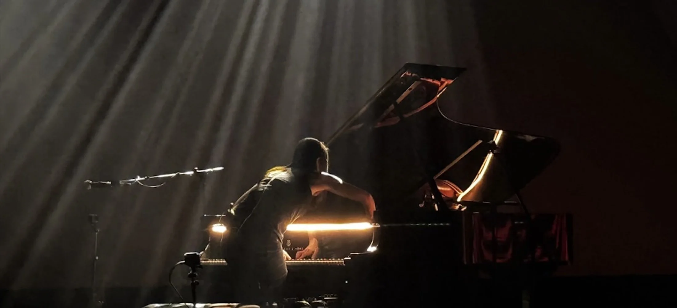 A person performing a piano concerto at the Double E VT on a grand piano under dramatic stage lighting with a dark background.