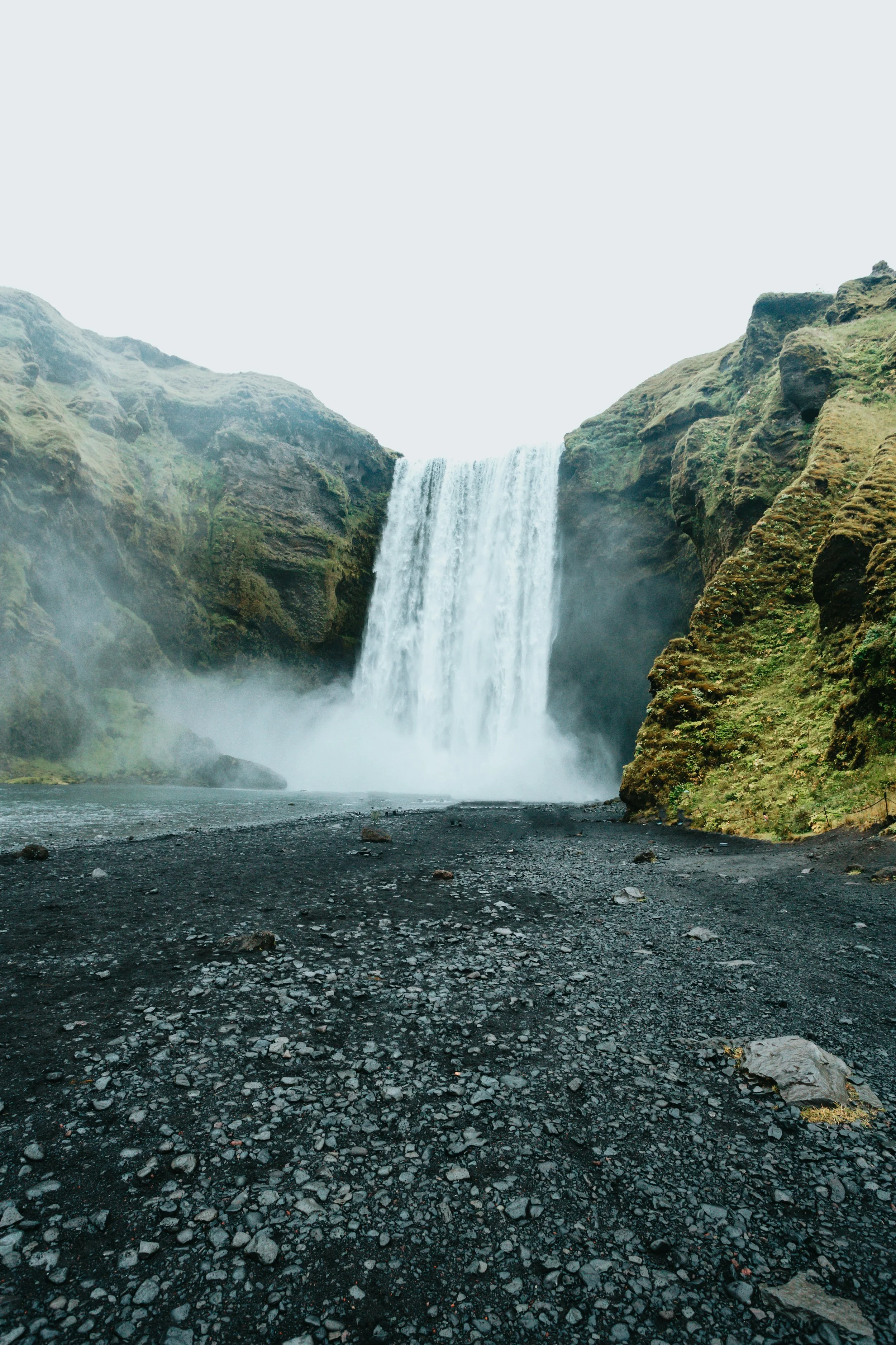 Waterfall cascading down moss-covered cliffs with black volcanic rocks at the base.