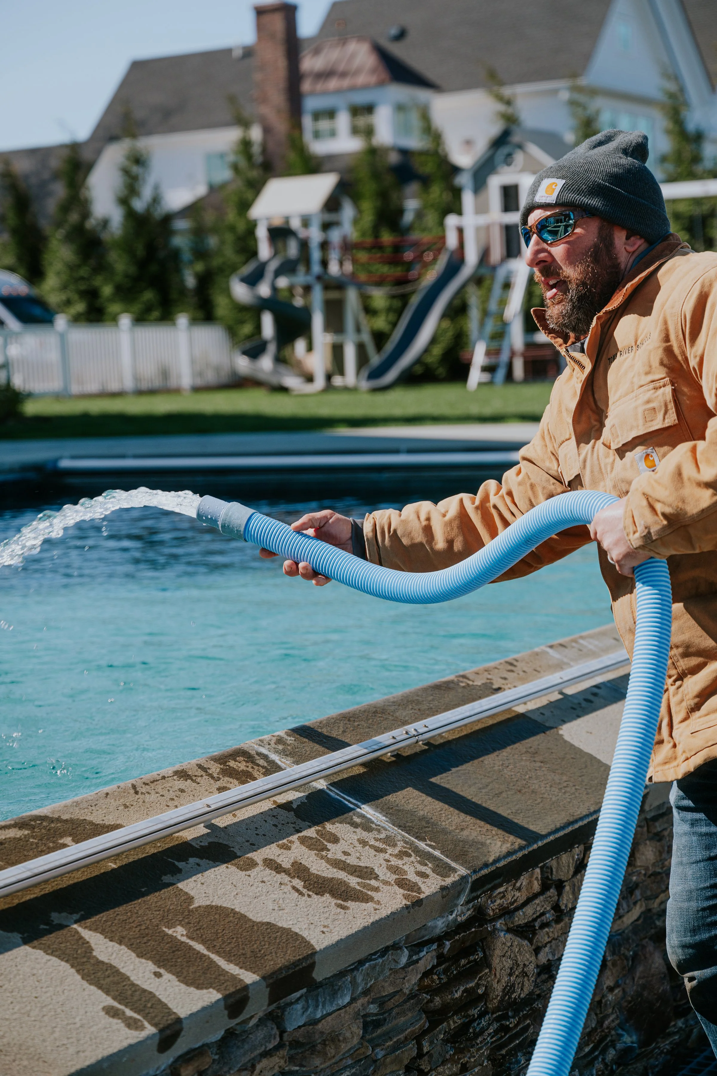 A man cleaning a swimming pool with a blue hose.